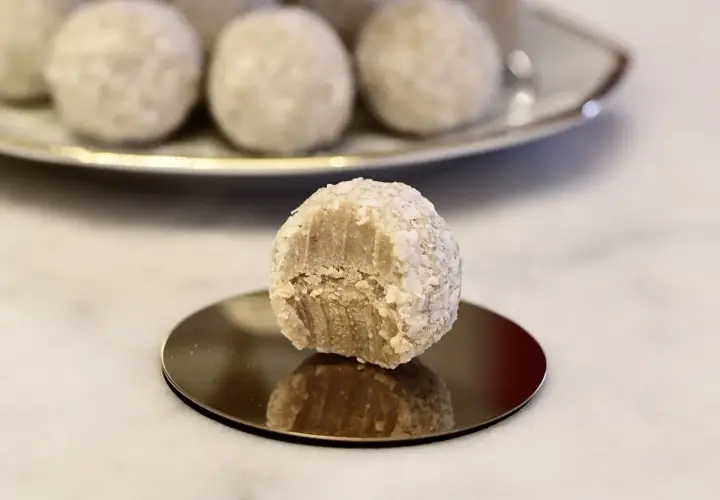En närbild på en bit av en vit chokladboll, rullad i kokosflingor, med fler chokladbollar i bakgrunden.