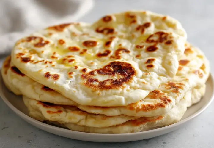 En hög med fluffigt, gyllene naanbröd, perfekt för ditt nästa naan recept. Smält smör glänser på toppen.