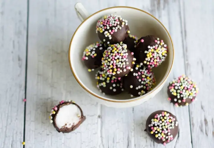 Chokladbollar med färgglatt strössel, perfekta för ett enkelt punschpraliner recept. En är uppskuren och visar ett vitt, fluffigt inre.