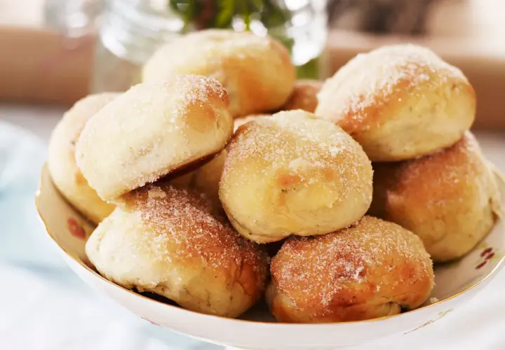 En skål med nybakade bullar, perfekt för att baka med söt jäst. De är pudrade med socker och ser aptitliga ut.