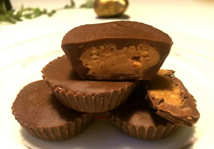 En hög med chokladkoppar med jordnötssmörsfyllning. En är uppskuren och visar den krämiga fyllningen.