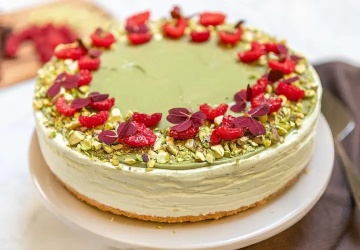 En krämig pistage cheesecake, dekorerad med hallon och pistagenötter. En dröm för alla sötsugna!