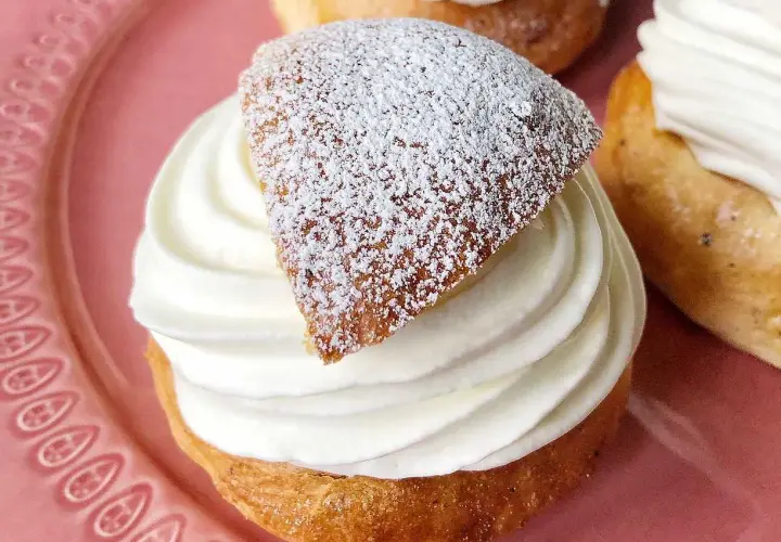 En gammaldags semla med fluffig grädde och pudrat lock på en rosa tallrik.