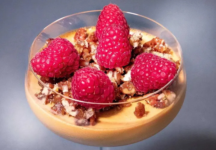 En krämig dulce de leche pannacotta toppad med färska hallon och nötter i ett glas.