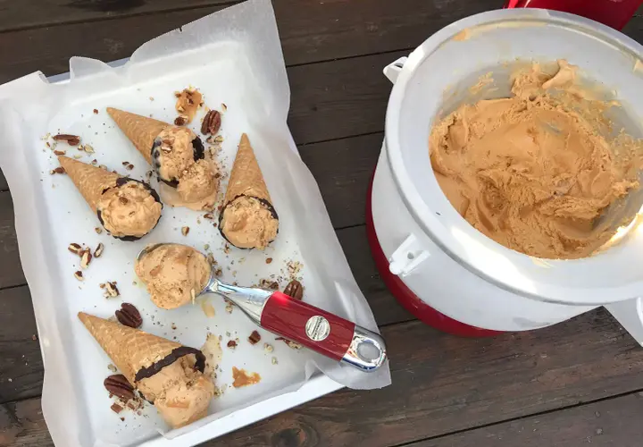 Färdiggjord dulce de leche glass i strutar, toppad med nötter och choklad. En skopa väntar bredvid glassmaskinen.
