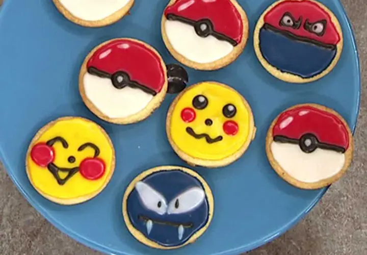 Sju dekorerade kakor på en blå tallrik, inklusive Pikachu, Pokémons och en Gastly. En härlig pokemon tårta för alla fans!