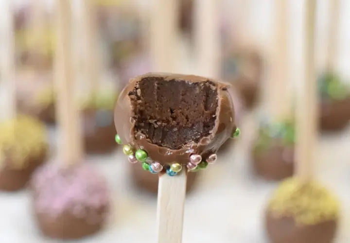 Chokladiga cake pops med färgglada strössel. En är uppäten och visar det saftiga inkråmet.