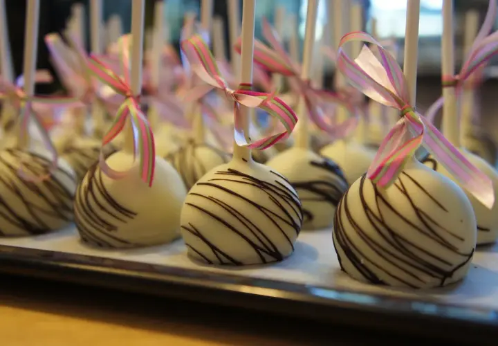 Vita cake pops med chokladmönster och rosa/gröna band. Perfekta för ett festligt tillfälle, som ett enkelt recept på oreo-bakverk.