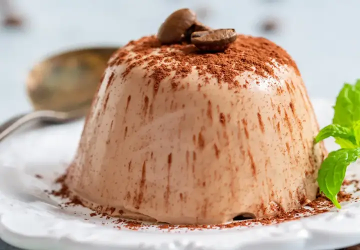 Krämig kaffepanna cotta toppad med kakaopulver och kaffebönor, garnerad med mynta.