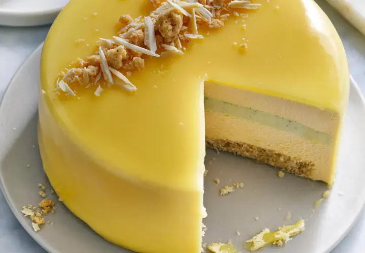 En vacker moussetårta med passionsfrukt, täckt av gul glasyr och toppad med smulor och vit choklad.