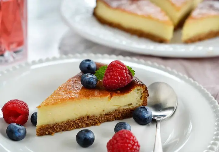 En bit krämig cheesecake med digestivebotten utan ugn, dekorerad med färska bär och mynta.