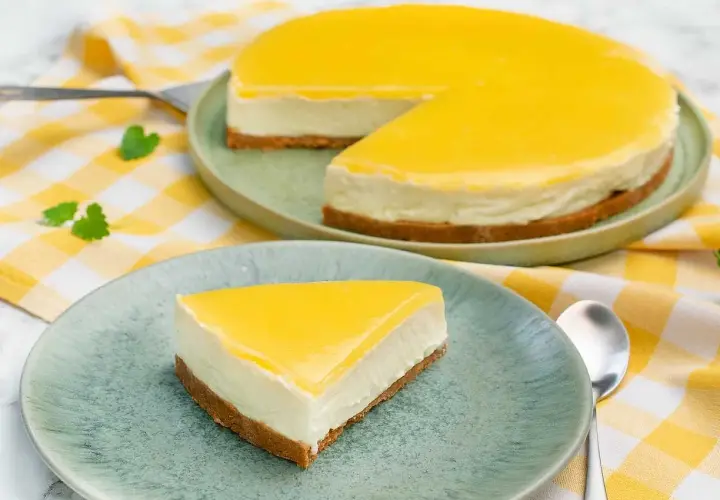 En krämig cheesecake med en syrlig lemon curd-topping, serverad på en ljusgrön tallrik med en gulrutig duk.