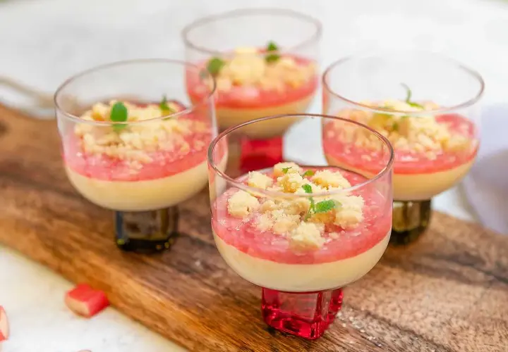 Fyra glas med krämig pannacotta med rabarberkompott och smuldeg. Garnerad med mynta. En härlig sommardessert.