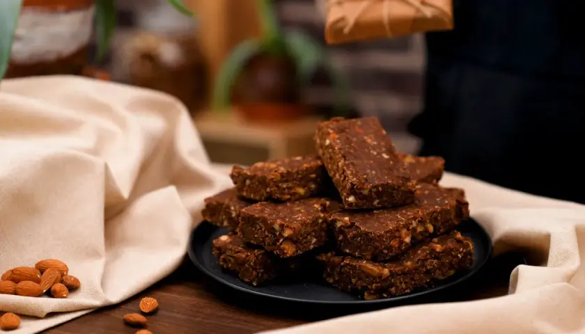 En hög med chokladdoppade dadlar och mandlar på en svart tallrik, omgivna av en ljus duk.