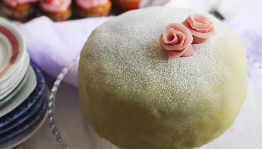 En grön prinsesstårta med rosa rosor, pudrad med florsocker. Perfekt för att fråga hur länge håller prinsesstårta i kylen.