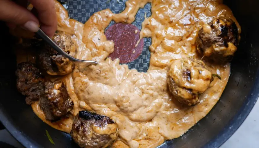 Köttbullar i krämig sås, perfekt tjocknad med maizena istället för potatismjöl. En gaffel rör om i den gyllene såsen.