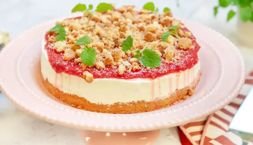 En läcker vit choklad cheesecake med hallon och smulor, dekorerad med mynta. Perfekt för fikat!