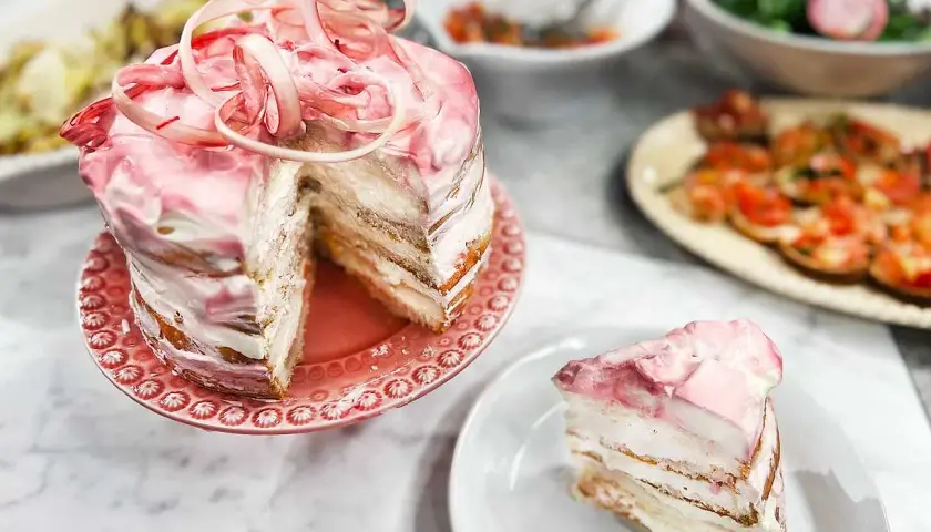 En vacker rabarberkompott tårta med rosa frosting och en skiva upplagd. Perfekt för en somrig fika.