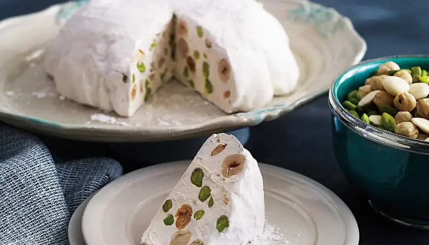 En bit av en vit nougatkaka med nötter och pistagenötter, perfekt att baka med nougat.