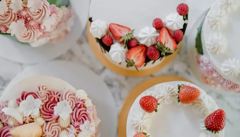 Flera vackra tårtor med fantasifulla dekorationer. En tårta är dekorerad med jordgubbar och maränger, en annan med rosa och vita blommor i frosting. Det är en festlig syn att dekorera tårta!