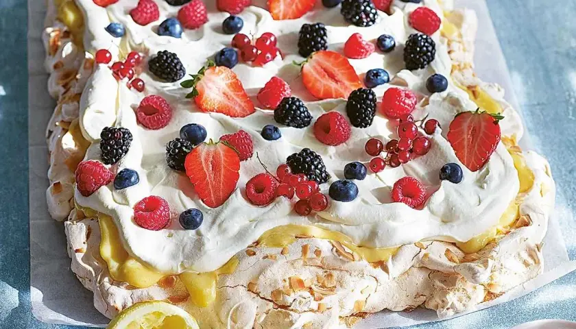 En stor pavlova i långpanna, täckt med vispgrädde, lemon curd och massor av färska bär som jordgubbar, hallon, blåbär och vinbär.