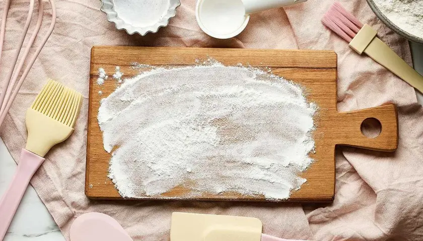 Bakredskap i pastellfärger ligger utspridda runt en skärbräda med mjöl, redo för bakning istället för vetemjöl.