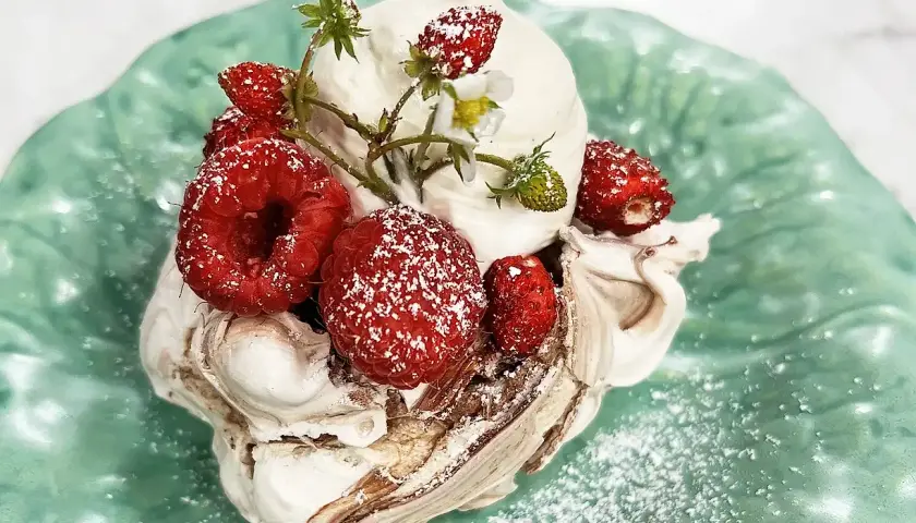 En härlig pavlova choklad med vispgrädde och färska bär, pudrad med florsocker på en grön tallrik.