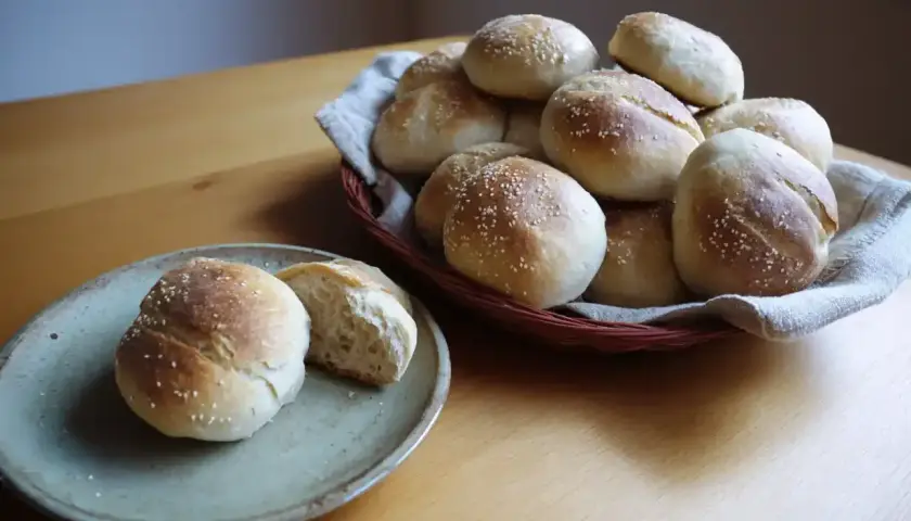 Nybakade bullar med sesamfrön, gjorda med rågsikt istället för vetemjöl. En del ligger i en korg, en annan på en tallrik.