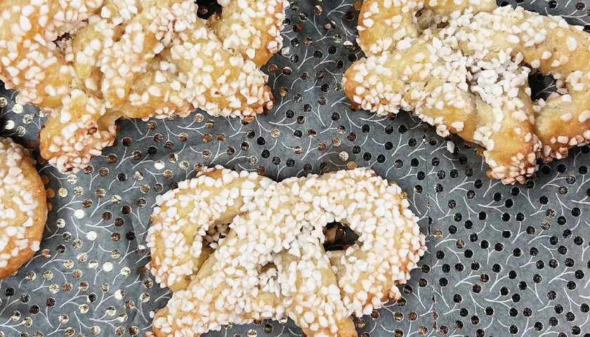 Gyllene kringlor täckta med socker strössel ligger på ett mönstrat underlag. Perfekta till fikat!