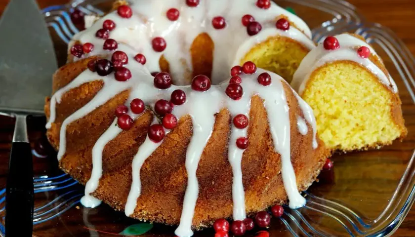 En saftig sockerkaka med sirap istället för socker, dekorerad med vit glasyr och färska lingon. En bit är uppskuren.
