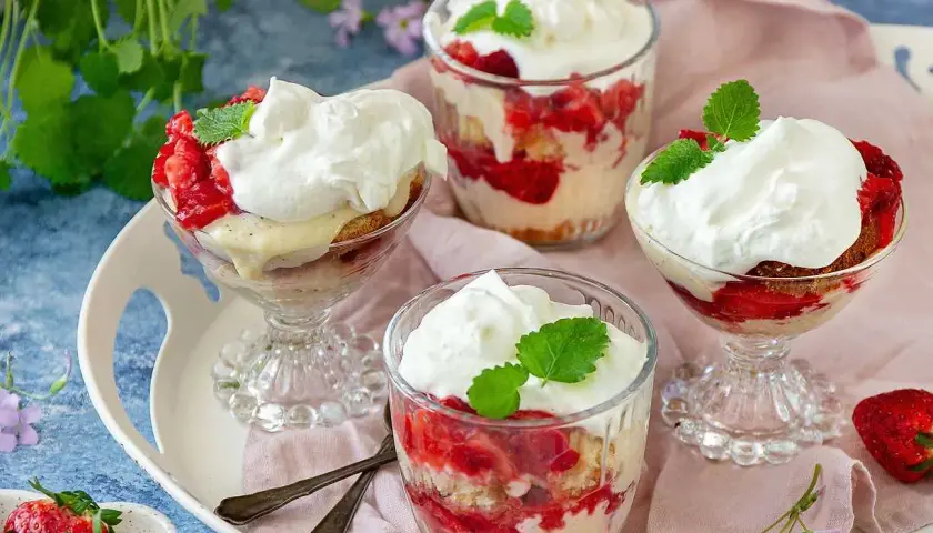 Ljuvlig jordgubbstårta i glas, lager av sockerkaka, färska jordgubbar och vispgrädde. Perfekt sommardessert.