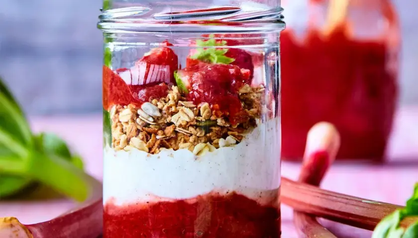 En glasburk med lager av rabarberkompott, yoghurt och granola. Rabarber är giftiga efter midsommar, men denna dessert är säker att njuta av.