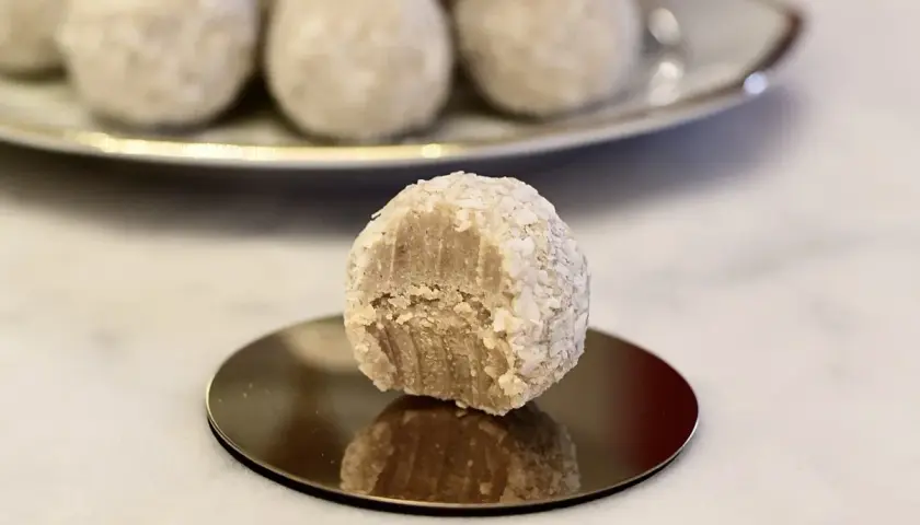 En närbild på en bit av en vit chokladboll, rullad i kokosflingor, med fler chokladbollar i bakgrunden.