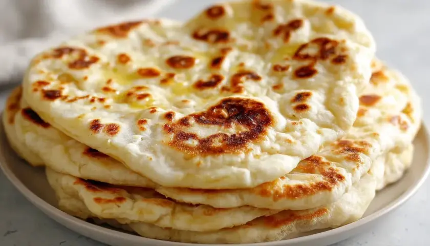 En hög med fluffigt, gyllene naanbröd, perfekt för ditt nästa naan recept. Smält smör glänser på toppen.
