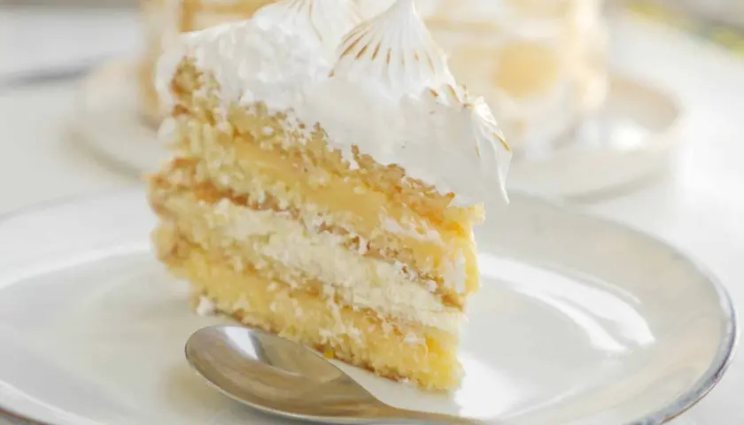 En bit fluffig lemoncurd tårta med marängtoppar på en vit tallrik med en sked.