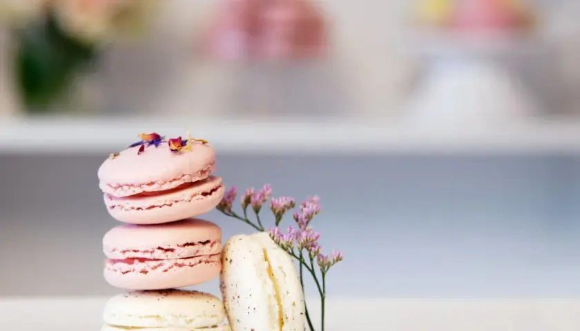 En stapel rosa och vita macarons, dekorerade med blomblad och en liten lila blomma. Perfekt för essenser bakning.