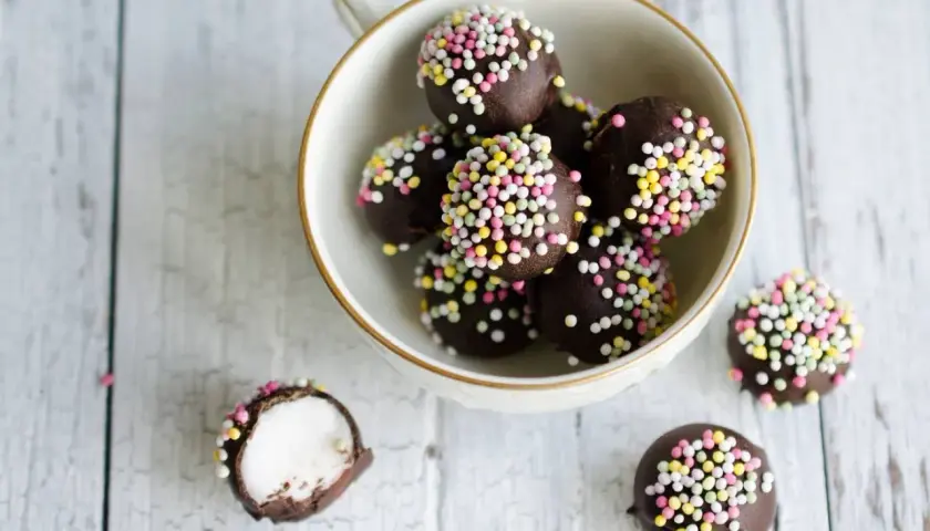 Chokladbollar med färgglatt strössel, perfekta för ett enkelt punschpraliner recept. En är uppskuren och visar ett vitt, fluffigt inre.