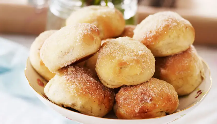 En skål med nybakade bullar, perfekt för att baka med söt jäst. De är pudrade med socker och ser aptitliga ut.