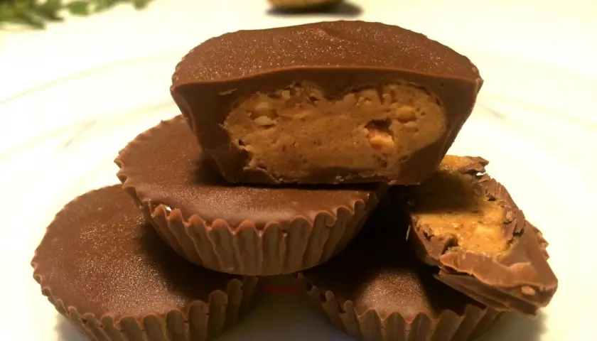 En hög med chokladkoppar med jordnötssmörsfyllning. En är uppskuren och visar den krämiga fyllningen.