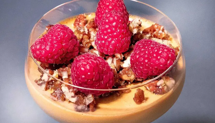 En krämig dulce de leche pannacotta toppad med färska hallon och nötter i ett glas.