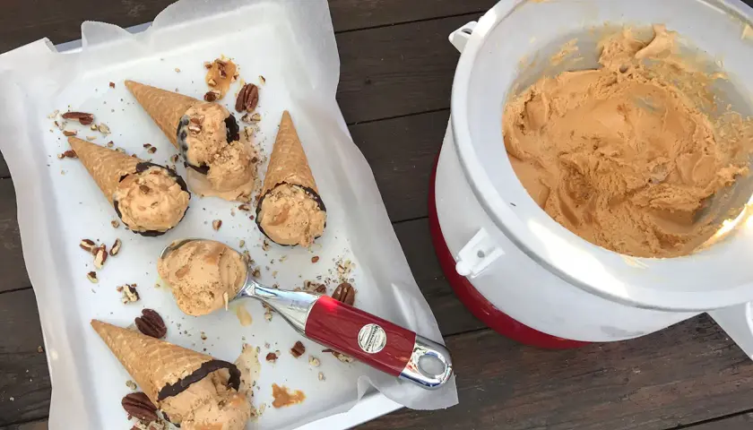 Färdiggjord dulce de leche glass i strutar, toppad med nötter och choklad. En skopa väntar bredvid glassmaskinen.