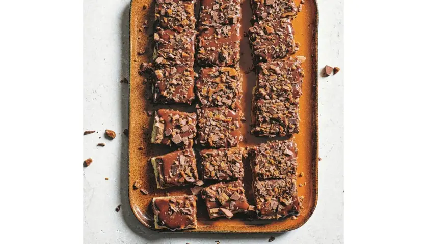 Chokladiga bitar av zserbó recept på en orange bricka, toppade med chokladglasyr och krossad choklad.