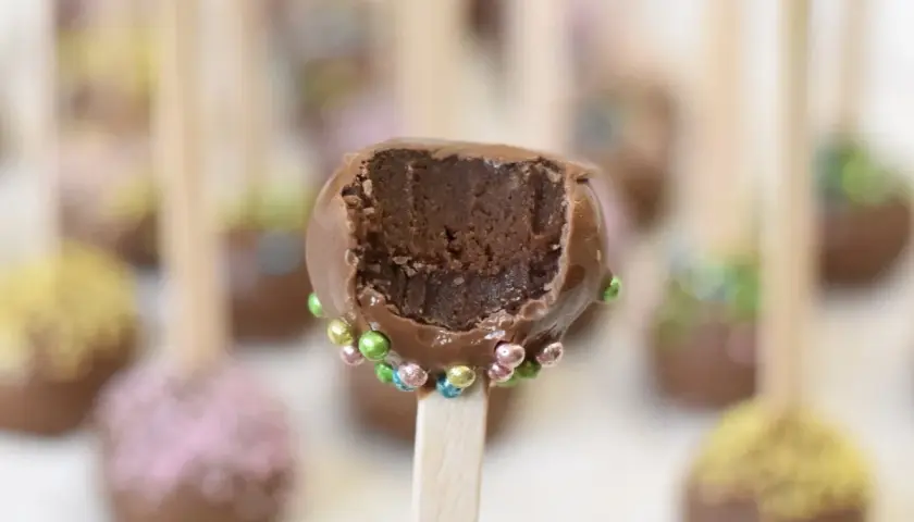 Chokladiga cake pops med färgglada strössel. En är uppäten och visar det saftiga inkråmet.