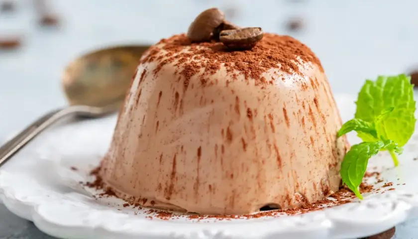 Krämig kaffepanna cotta toppad med kakaopulver och kaffebönor, garnerad med mynta.