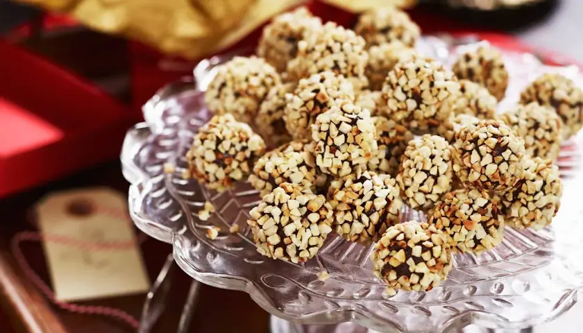 En hög med chokladtryffel täckta av hackade nötter på ett glasfat. Perfekt för fikat eller som en gåva.
