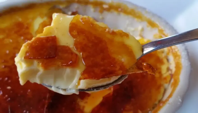 En sked lyfter en bit krämig creme brulee cheesecake med karamelliserat sockerlock.