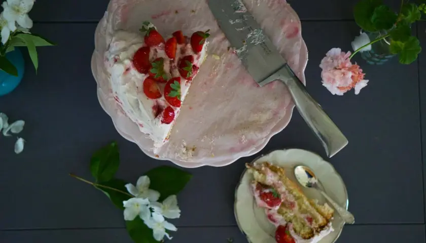 En bit av en läcker jordgubbstårta med grädde och färska jordgubbar. Ett perfekt jordgubbstårta recept för sommaren.