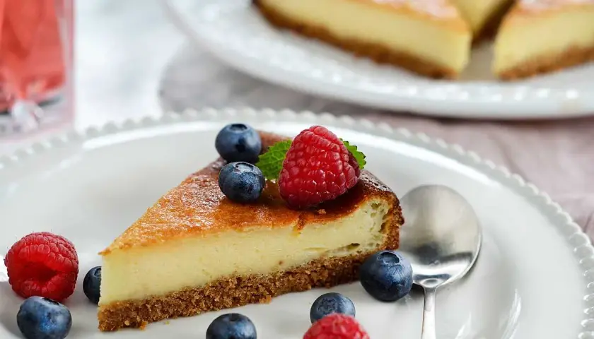 En bit krämig cheesecake med digestivebotten utan ugn, dekorerad med färska bär och mynta.
