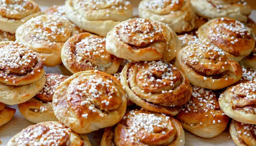 En hög med gyllene kanelbullar, toppade med pärlsocker. Perfekt för fikat, här är ett enkelt kanelbullar recept.