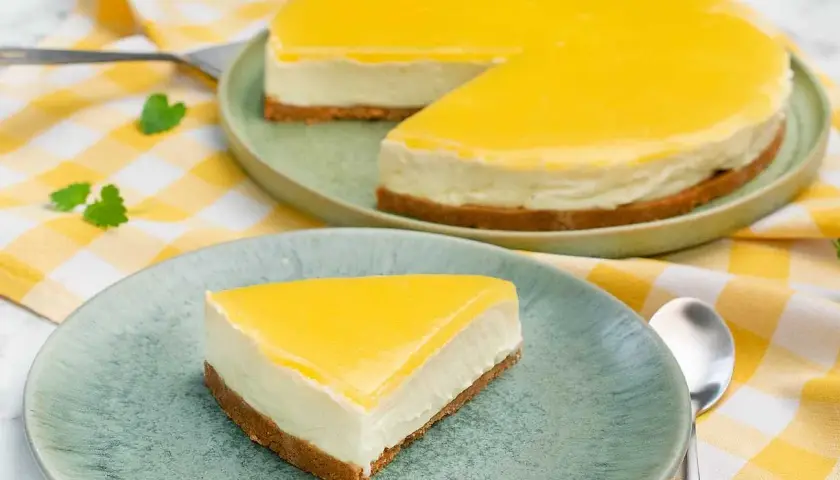 En krämig cheesecake med en syrlig lemon curd-topping, serverad på en ljusgrön tallrik med en gulrutig duk.